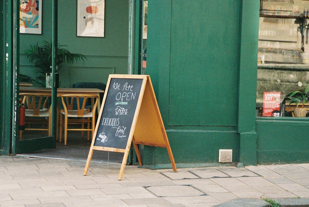 A chalkboard sign reading We Are OPEN on a sidewalk outside a green cafe